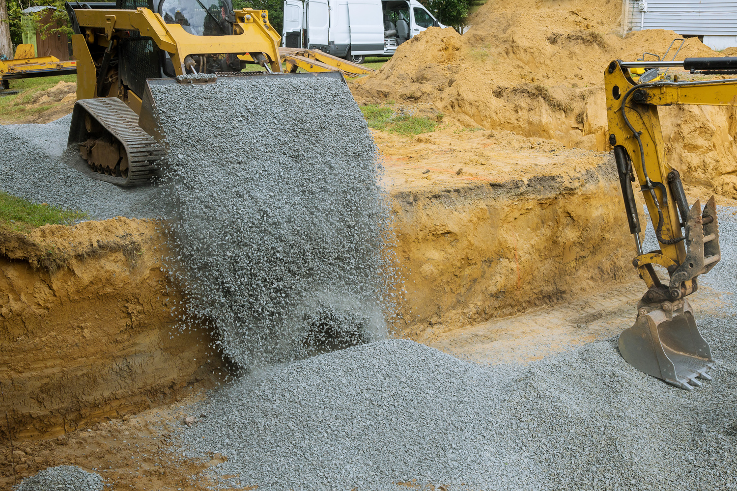 Excavator bucket backfilling trench for stone backfill of foundation